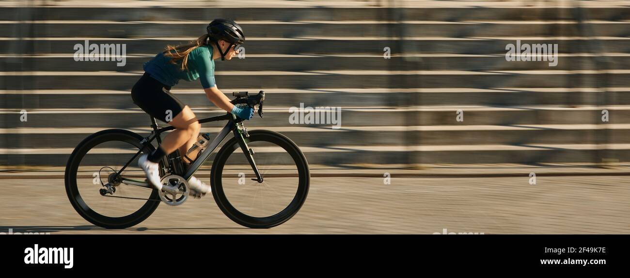 Intestazione del sito web di vista laterale del ciclista femminile professionista in abbigliamento da ciclismo e attrezzatura protettiva in bicicletta in città, corsa e passaggio Foto Stock