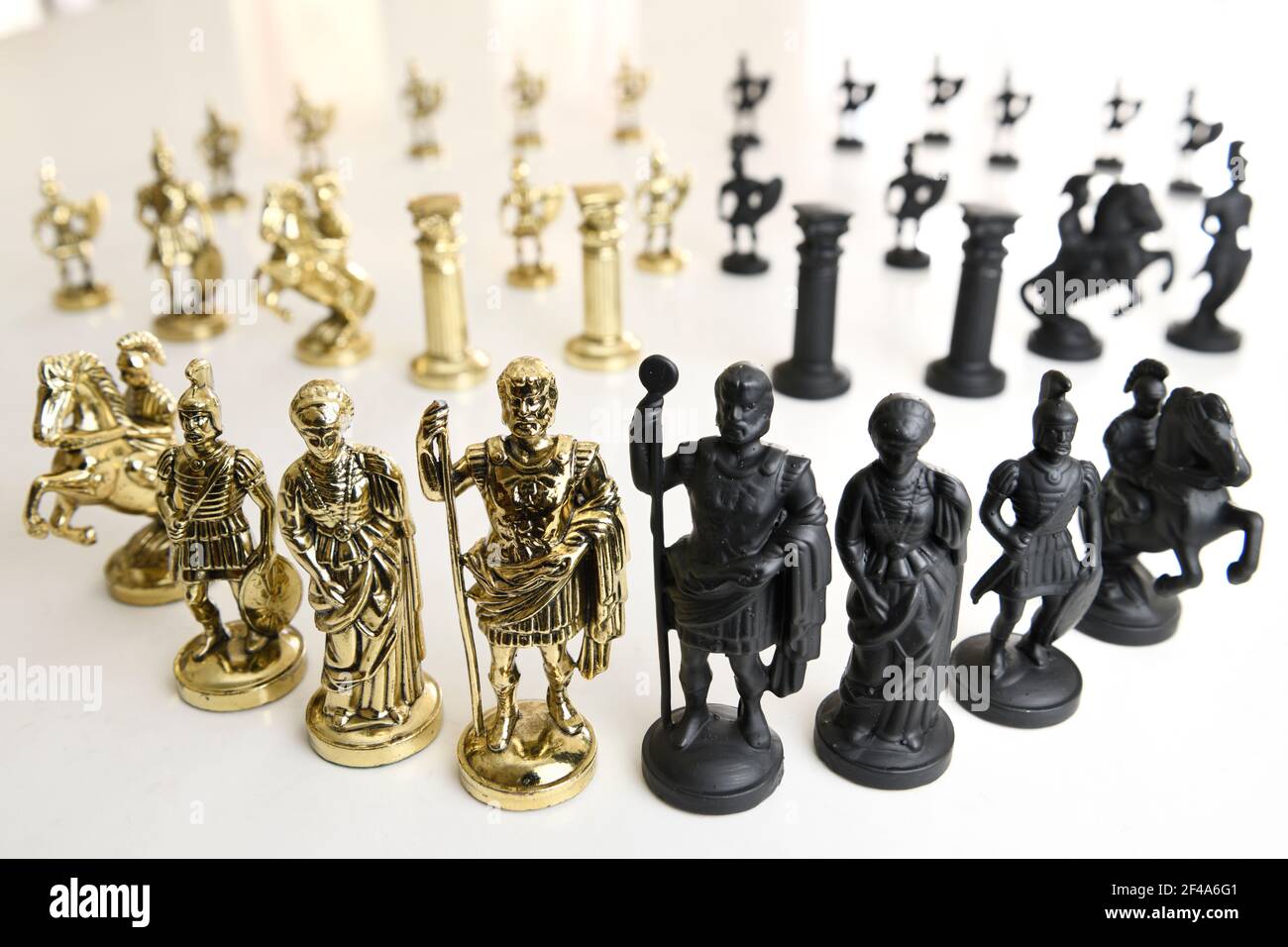 Eserciti contrapposti in nero e oro di pezzi di scacchi figuranti in metallo su sfondo bianco Foto Stock
