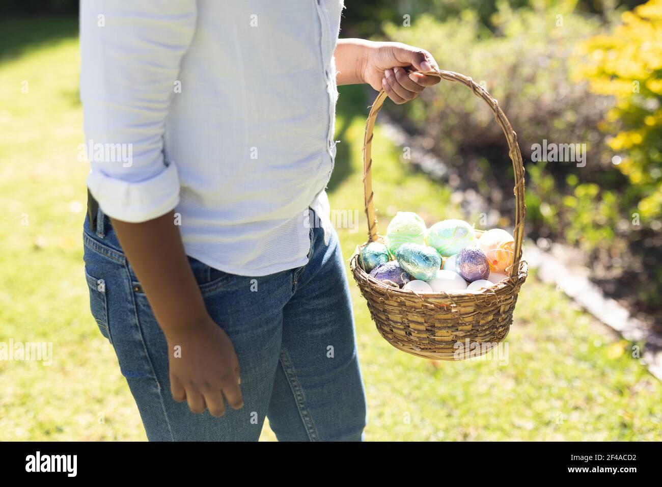 Sezione centrale del ragazzo afroamericano che tiene il cestino mentre uovo di pasqua caccia Foto Stock