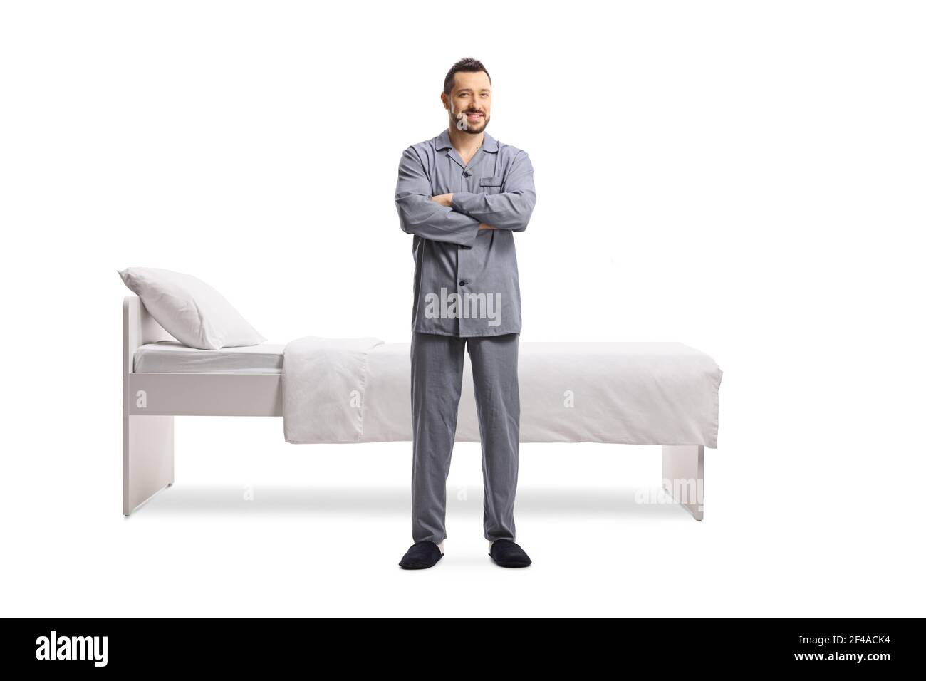 Ritratto a lunghezza intera di un giovane in pigiama in piedi di fronte ad un letto singolo isolato su sfondo bianco Foto Stock