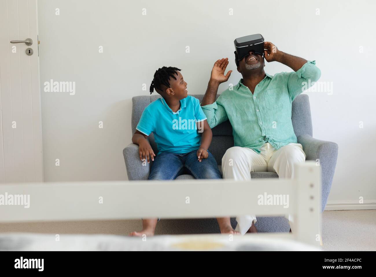 Nonno africano americano senior con visore vr seduto sul divano accanto al nipote sorridente Foto Stock