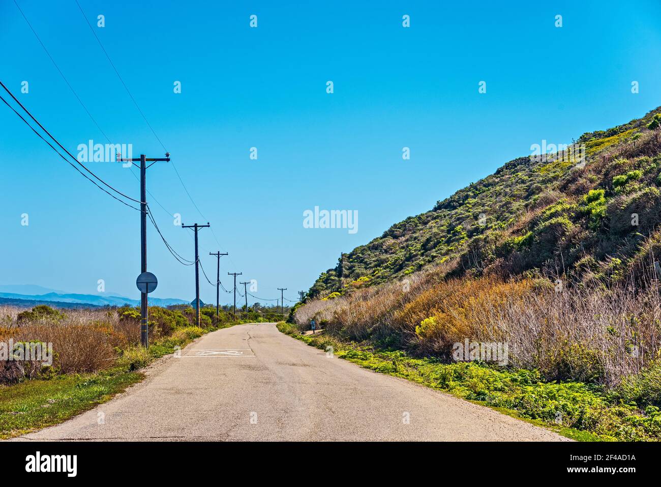 Il pavimento si curva intorno alla collina fiancheggiata da pali telefonici sotto il cielo blu. Foto Stock