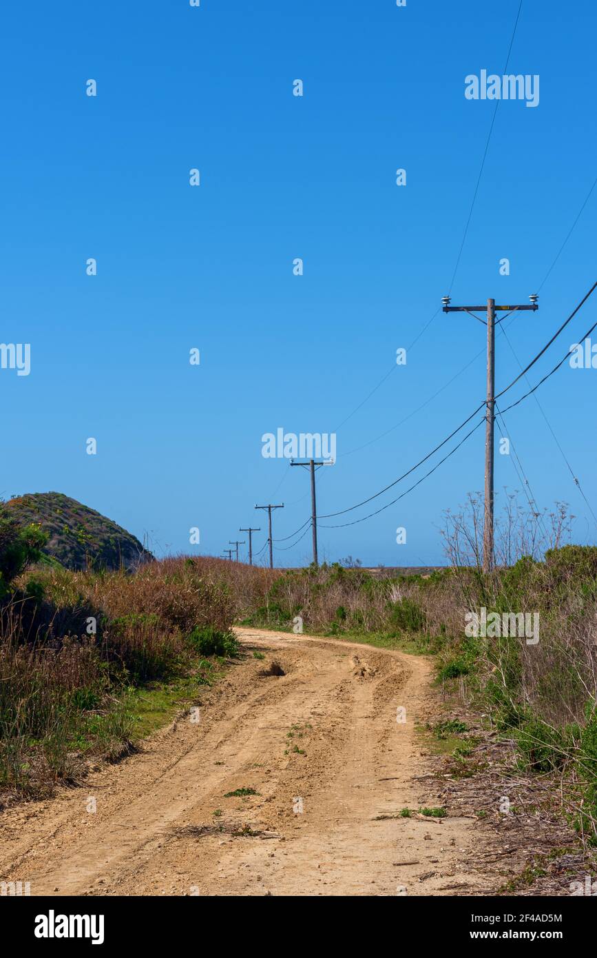 La strada sterrata si curva intorno alle colline erbose e attraverso i campi fiancheggiati da pali telefonici sotto il cielo blu. Foto Stock