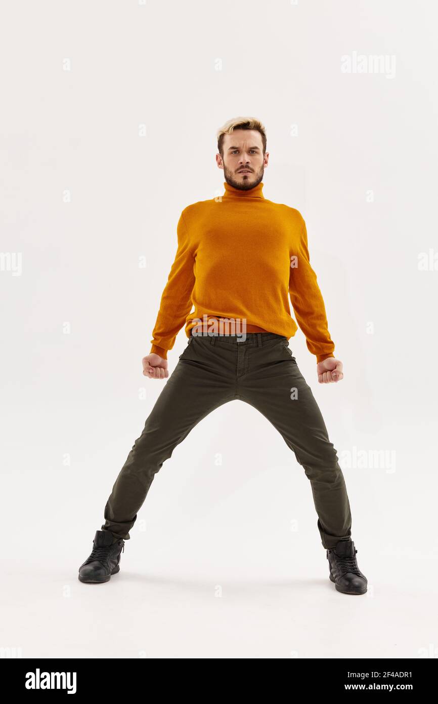 modello maschile in un maglione arancione allarga le gambe a parte su un  paio di pantaloni di sfondo chiaro Foto stock - Alamy