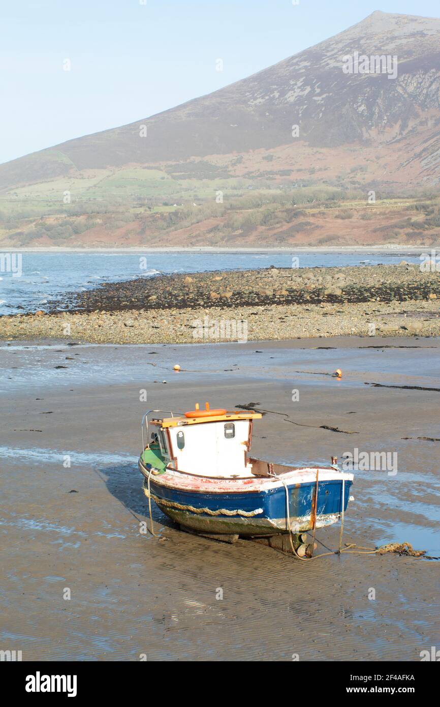 Trefor, Galles. Lone barca da pesca sulla spiaggia a bassa marea. Scatto verticale con sfondo di montagne lontane. Vista verticale e spazio di copia. Foto Stock