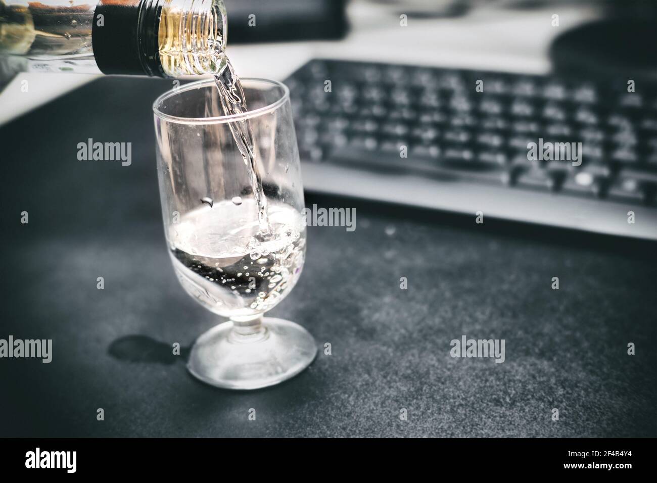 Ubriaco al lavoro. Versare un bicchiere di vodka. Scrivania e tastiera offocate per mostrare una visione e una funzionalità cerebrali compromesse. Concetto per affrontare con wor Foto Stock