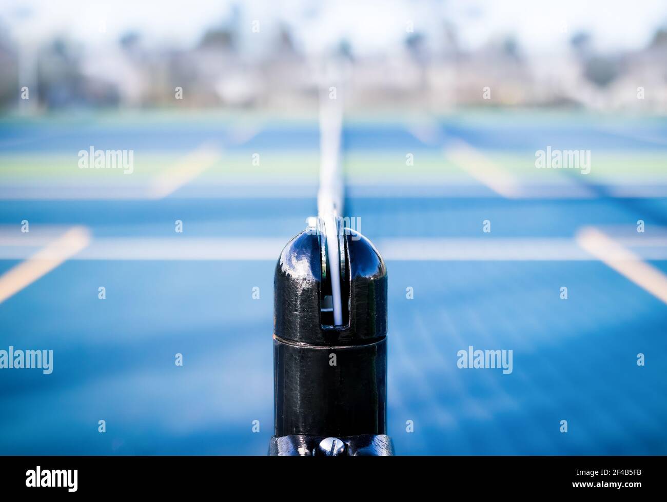 Campo da tennis astratto struttura sportiva, fuori mattina presto. Palo in rete nero con rete sfocata, linee da campo da tennis, rubberiz blu e verde Foto Stock