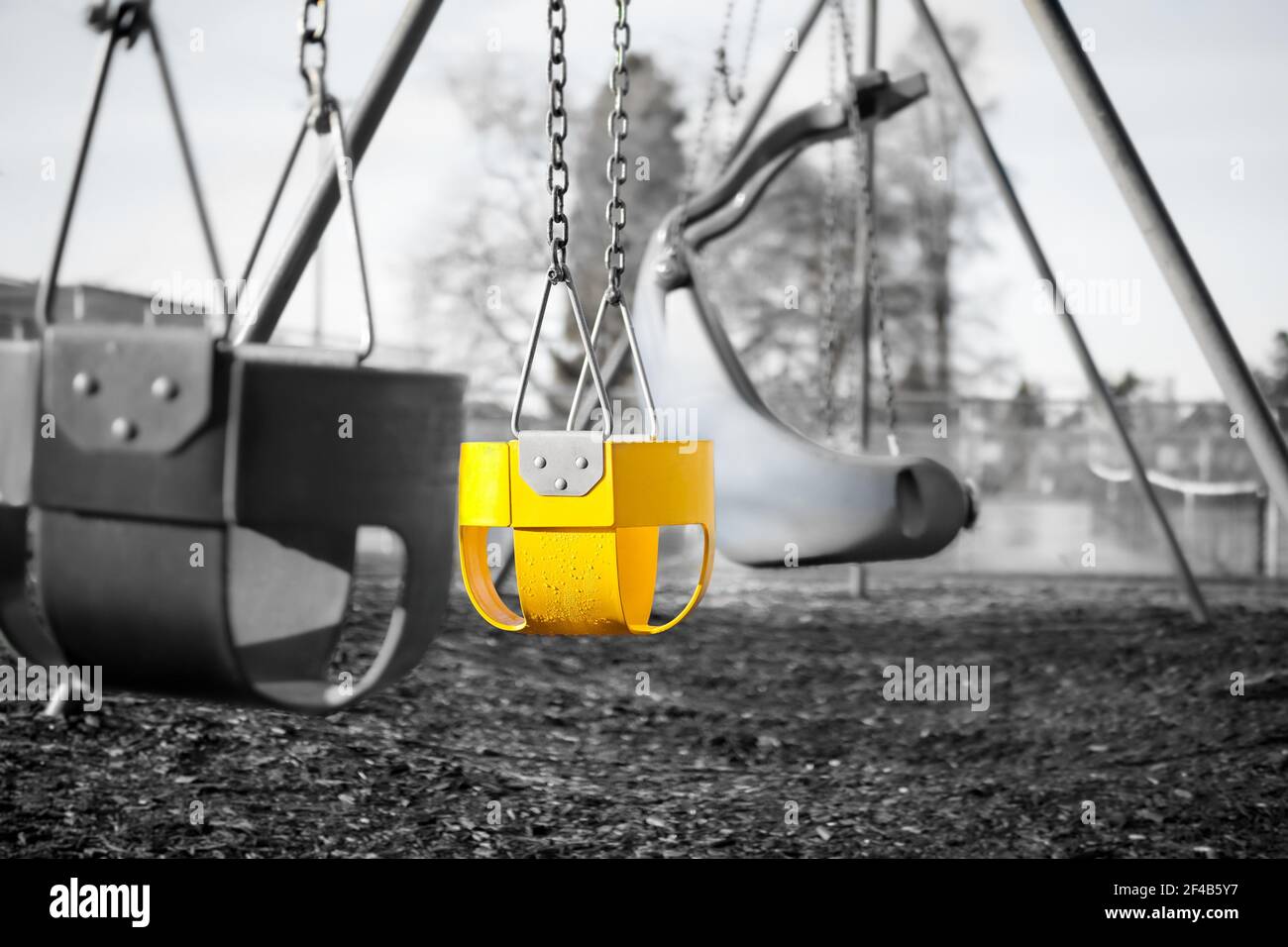 Parco giochi per bambini con sedili a secchio completi, primo piano. Immagine in bianco e nero con un sedile di colore giallo brillante. Colore selettivo Foto Stock