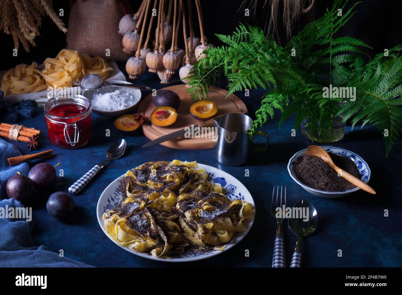 Pasta dolce dessert, tagliatelle con semi di papavero, prugna composta di prugne fresche, sfondo scuro, tavolo blu decorato con fiori freschi. Tutto secco popp Foto Stock