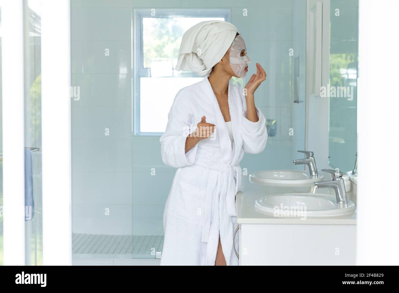 Misto razza donna che indossa accappatoio e pulizia maschera viso in bagno Foto Stock