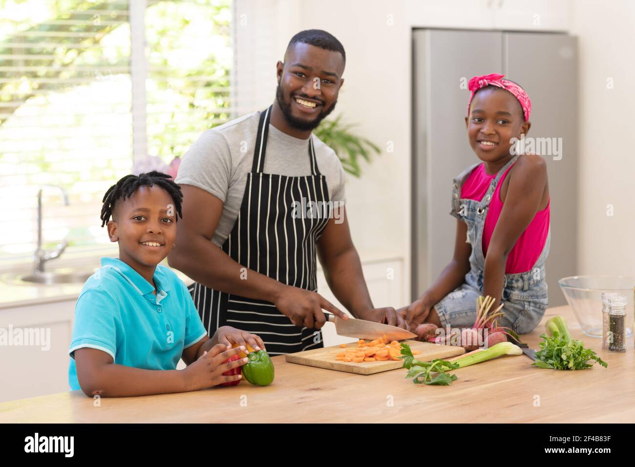 Felice padre afroamericano insegnando figlia e figlio che cucinano dentro la cucina Foto Stock