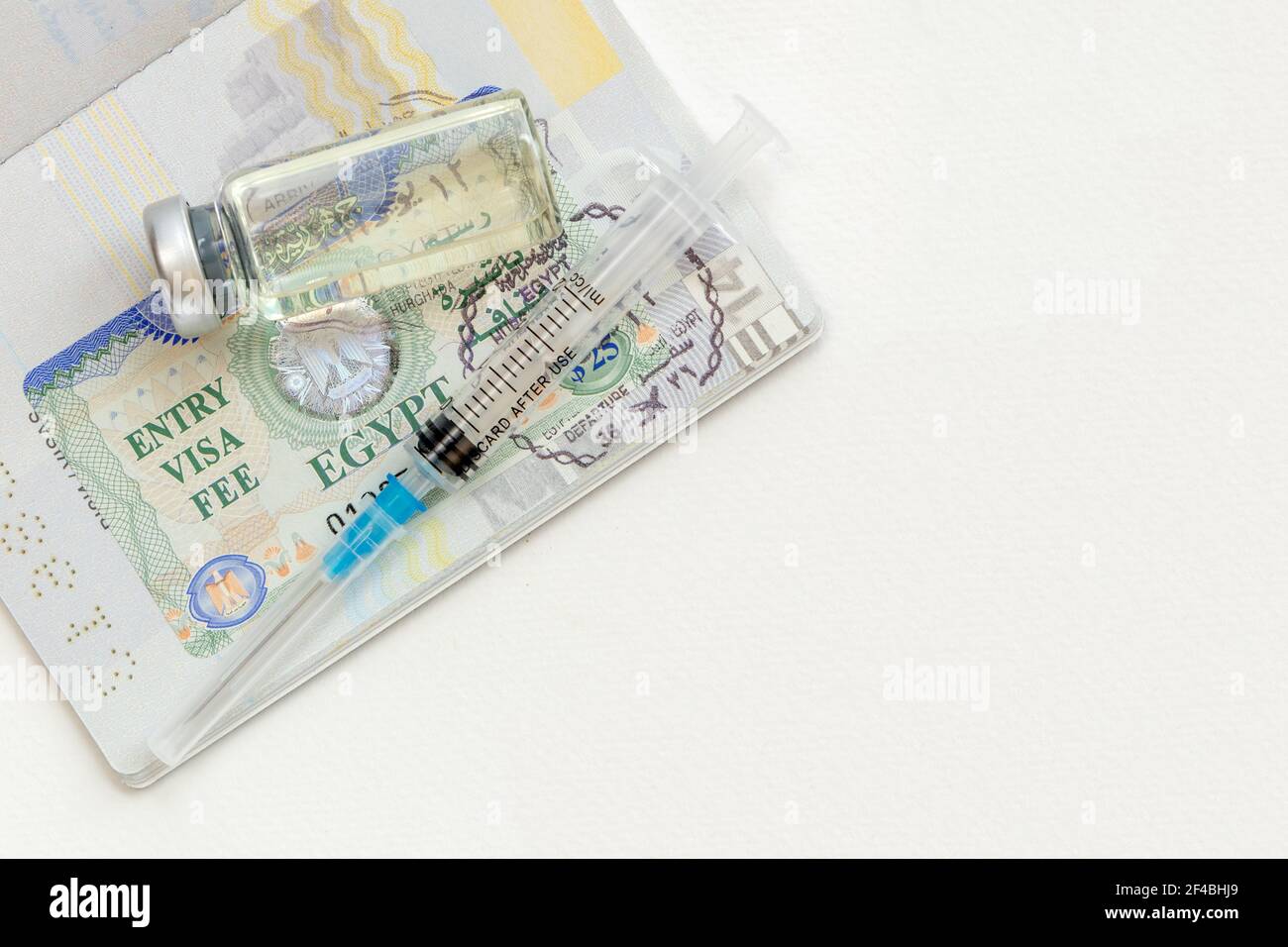 Siringa con ago, flaconcino e passaporto con visto di ingresso egiziano su un tavolo bianco pronto per l'uso. Concetto di vaccinazione prima del viaggio. Foto Stock