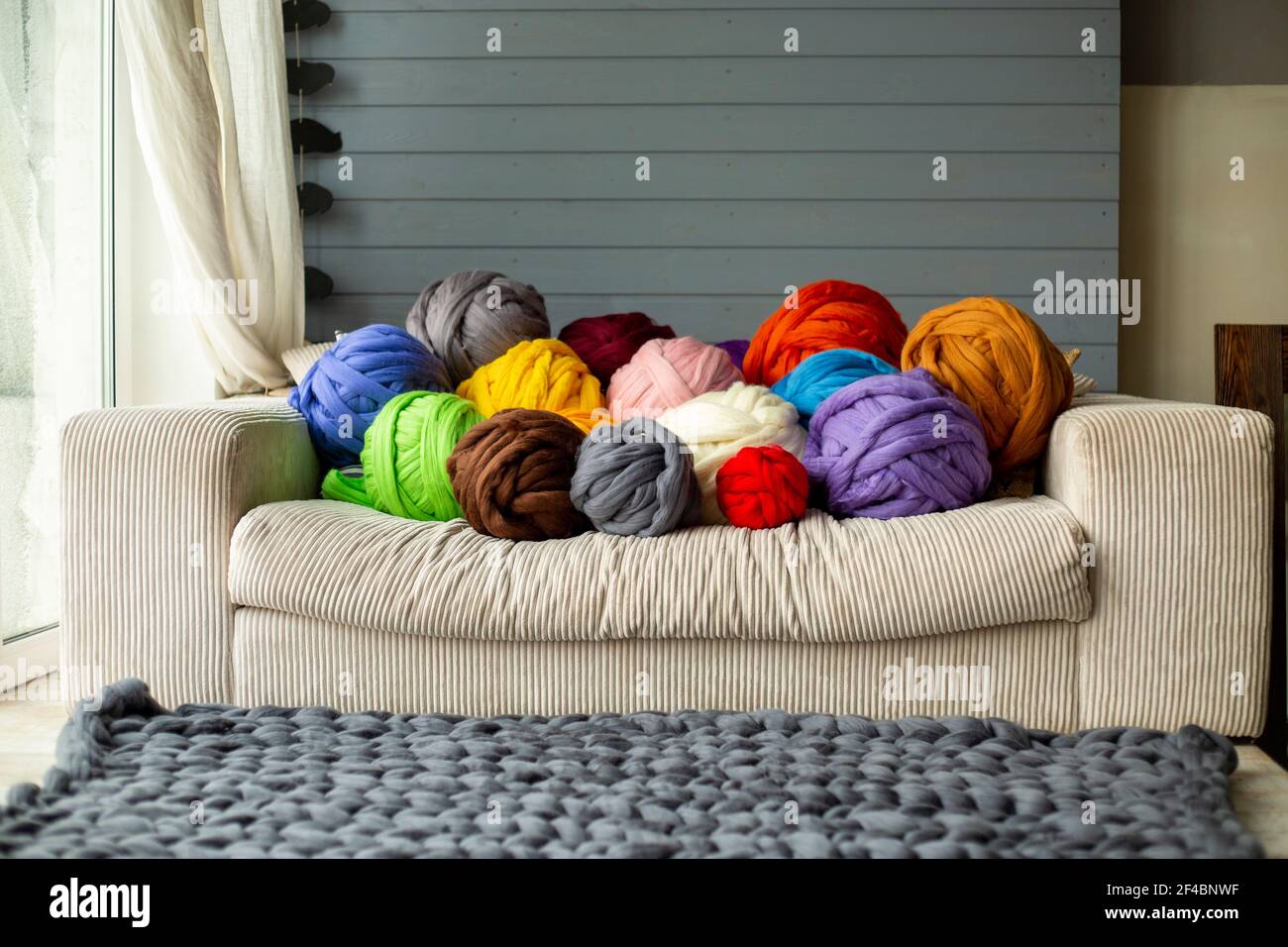 Palline colorate di lana merino sul divano vicino alla finestra con una plaid grigia in una giornata di sole. Foto Stock
