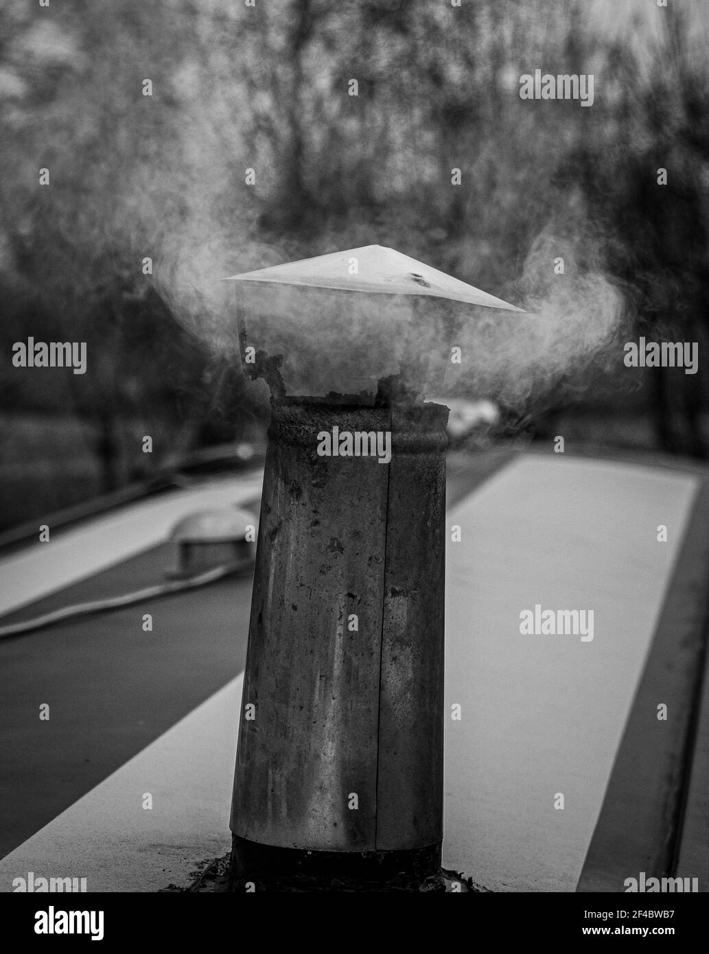 Bianco e nero monocromatico di fumo che esce dal camino su una narrowboat con fondo bokeh piano Foto Stock