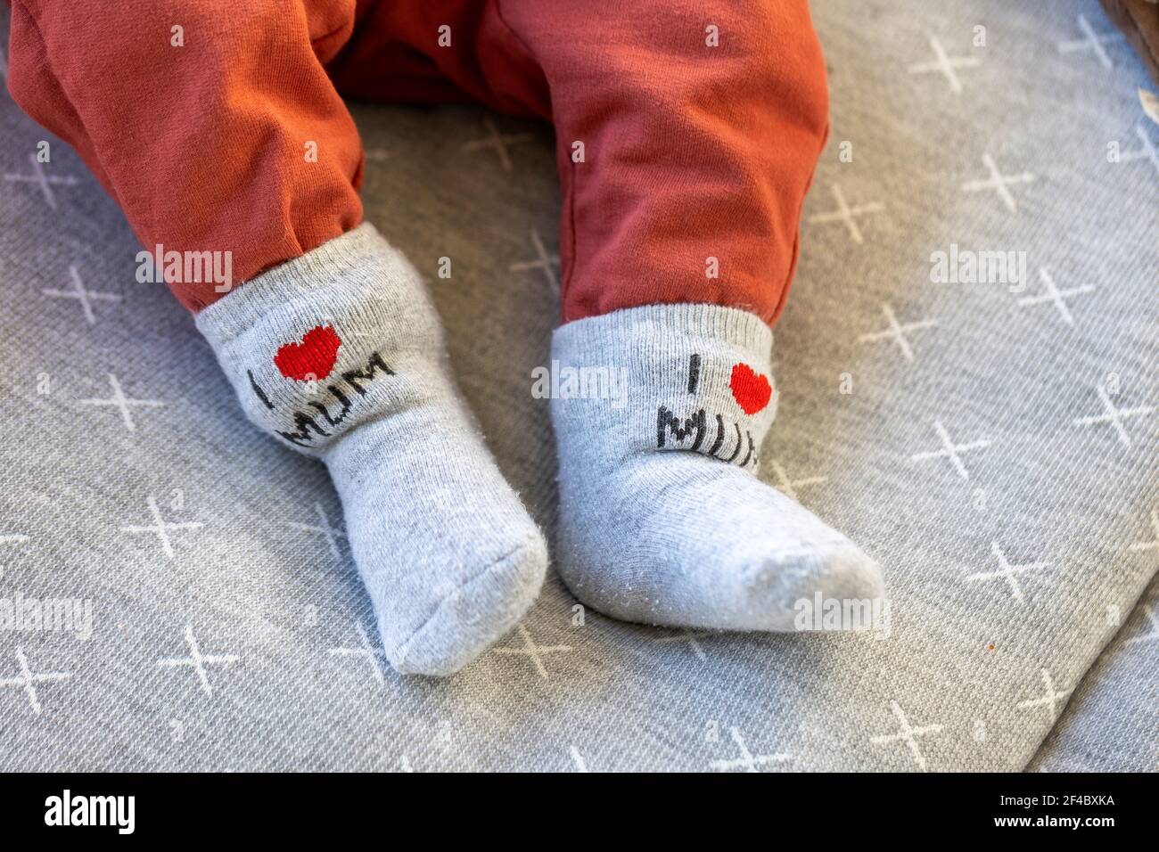 Un ritratto dei piedi di un bambino con calze grigie con, amo la mamma,  scritto su di loro e pantaloni. Il bambino è sdraiato su un cuscino grigio  Foto stock - Alamy