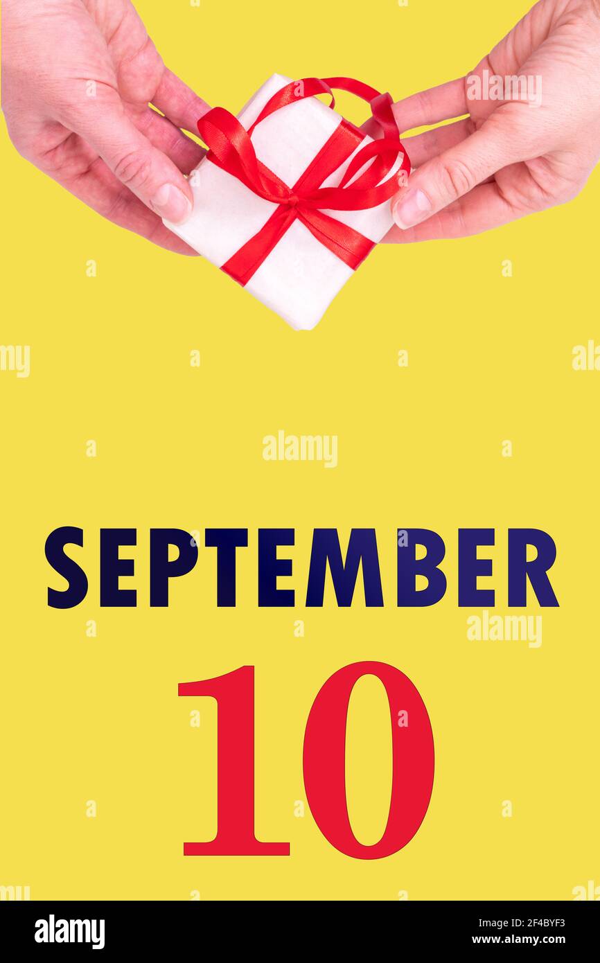 10 settembre. Calendario verticale festivo con mani in mano Bianco confezione regalo con nastro rosso e calendario Data 10 settembre su illuminante giallo schiena Foto Stock