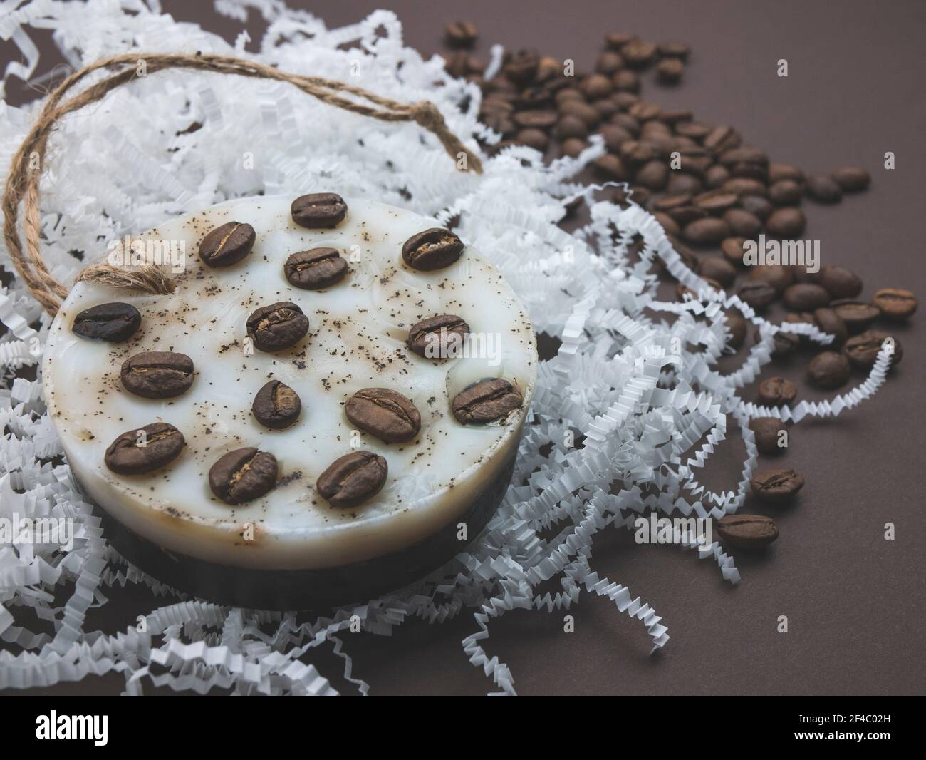 Caffè naturale fatto a mano profumato sapone rotondo sullo sfondo di carta bianca grattugiata e chicchi di caffè, primo piano Foto Stock
