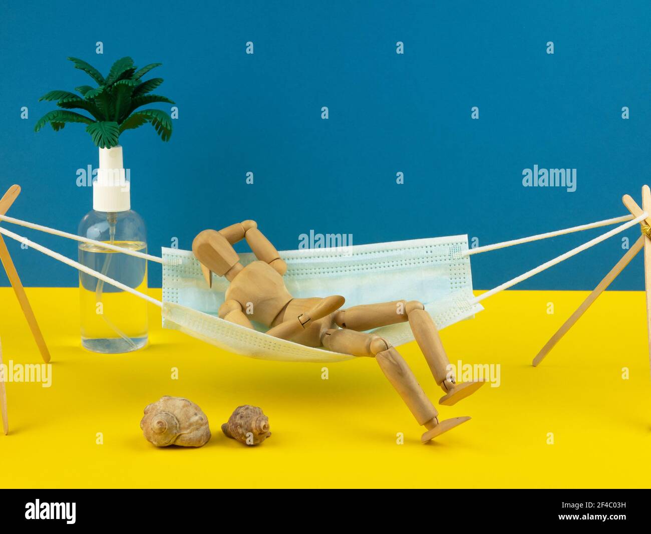 L'uomo giocattolo giace in amaca sotto forma di maschera medica. Concetto di vacanza, resort e turismo in una pandemia. Stile di vita del coronavirus Foto Stock