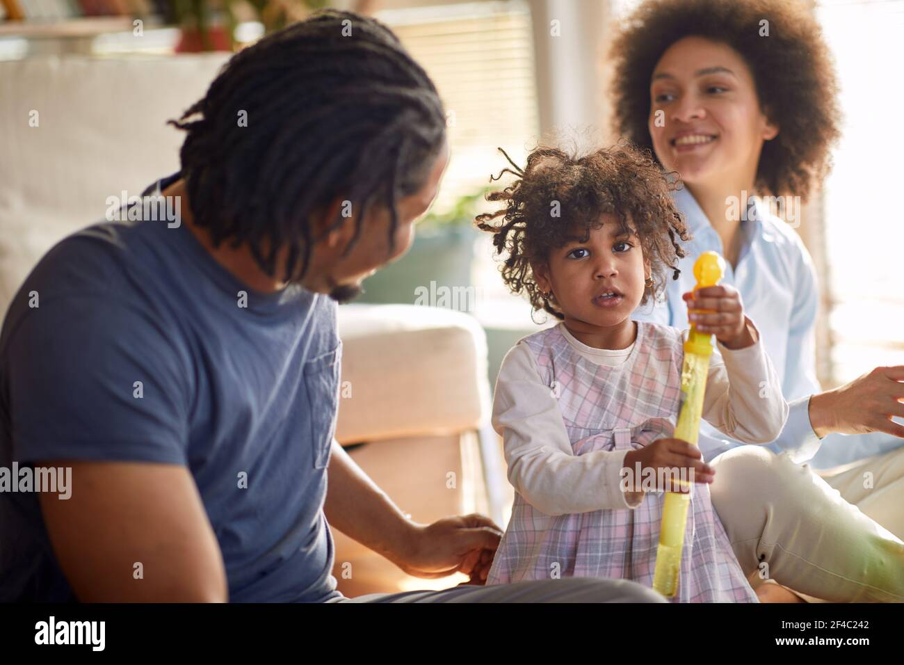Una bambina carina che posa per una foto mentre gioca con i suoi genitori in un'atmosfera divertente a casa. Famiglia, insieme, tempo di gioco Foto Stock