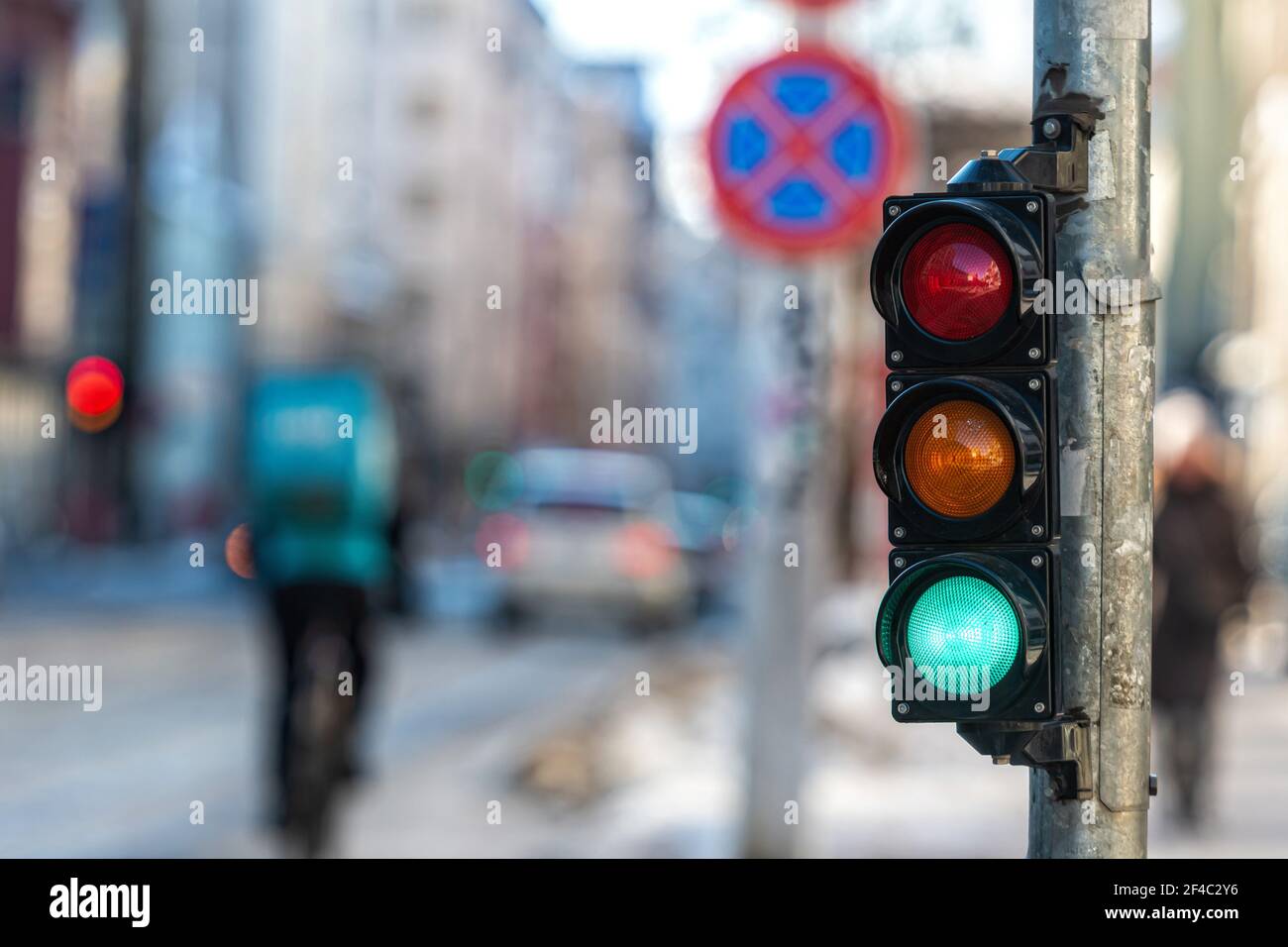 primo piano di un piccolo semaforo di traffico con semaforo verde contro il sfondo del traffico cittadino Foto Stock