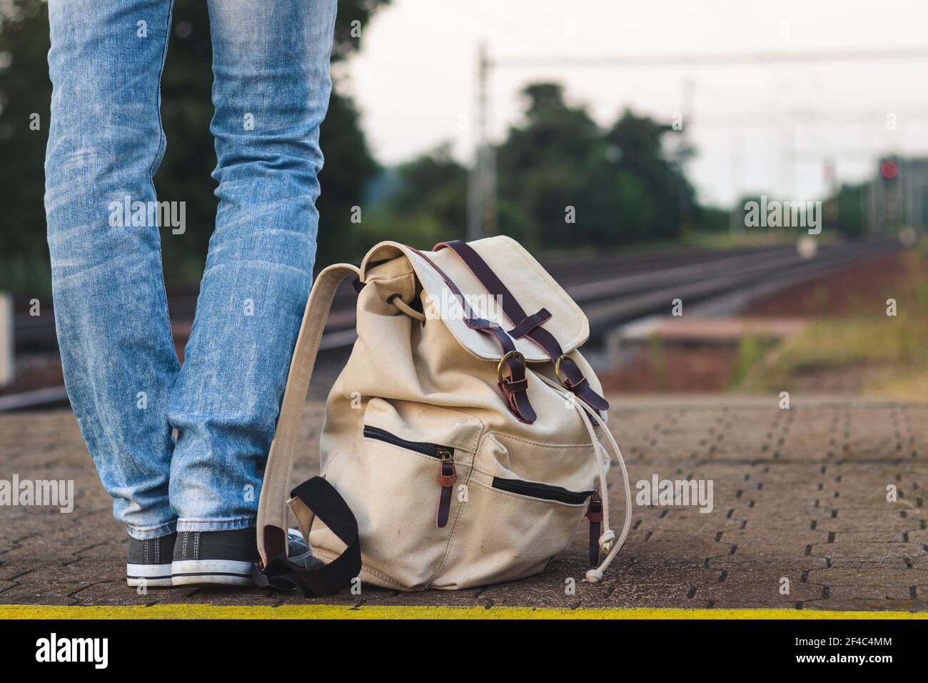 Backpacker in attesa di treno alla stazione ferroviaria. Donna che indossa jeans in piedi sulla piattaforma della stazione ferroviaria. Foto Stock