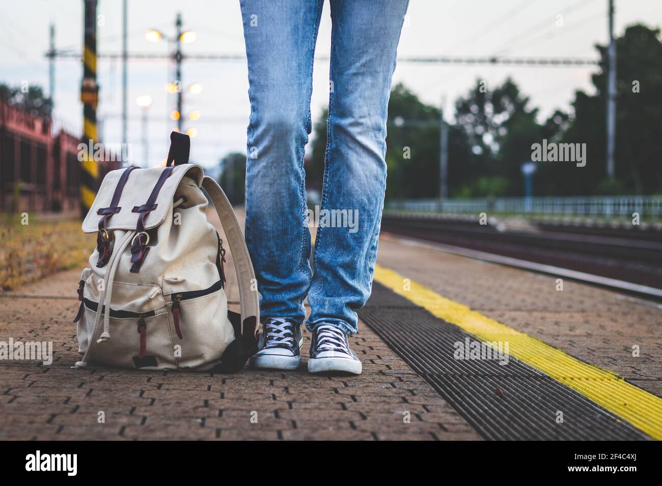 Viaggiatore in attesa di treno sulla stazione ferroviaria di mattina presto. Gambe e zaino femmina sulla piattaforma della stazione ferroviaria. Concetto di viaggio Foto Stock