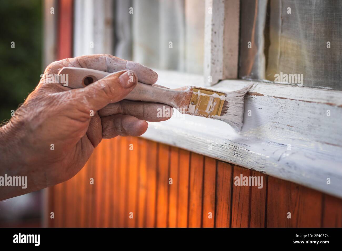 Vecchio uomo´s verniciatura a mano del serramento in legno con pennello. Riparazione esterno della capanna di legno Foto Stock