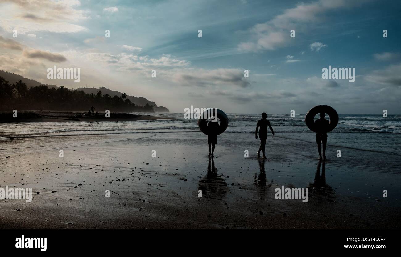 I ragazzi portano i tubi interni sulla spiaggia come tramonto a Palomino, Colombia. Foto Stock