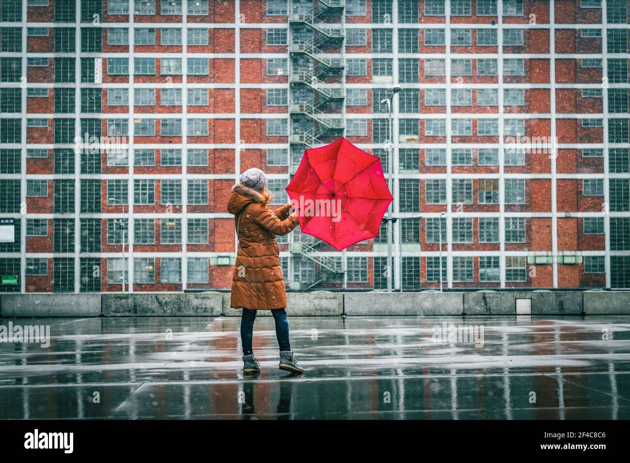 Donna con ombrello rosso in piedi in città durante la nevica. Architettura urbana prima della guerra in Europa. Foto Stock