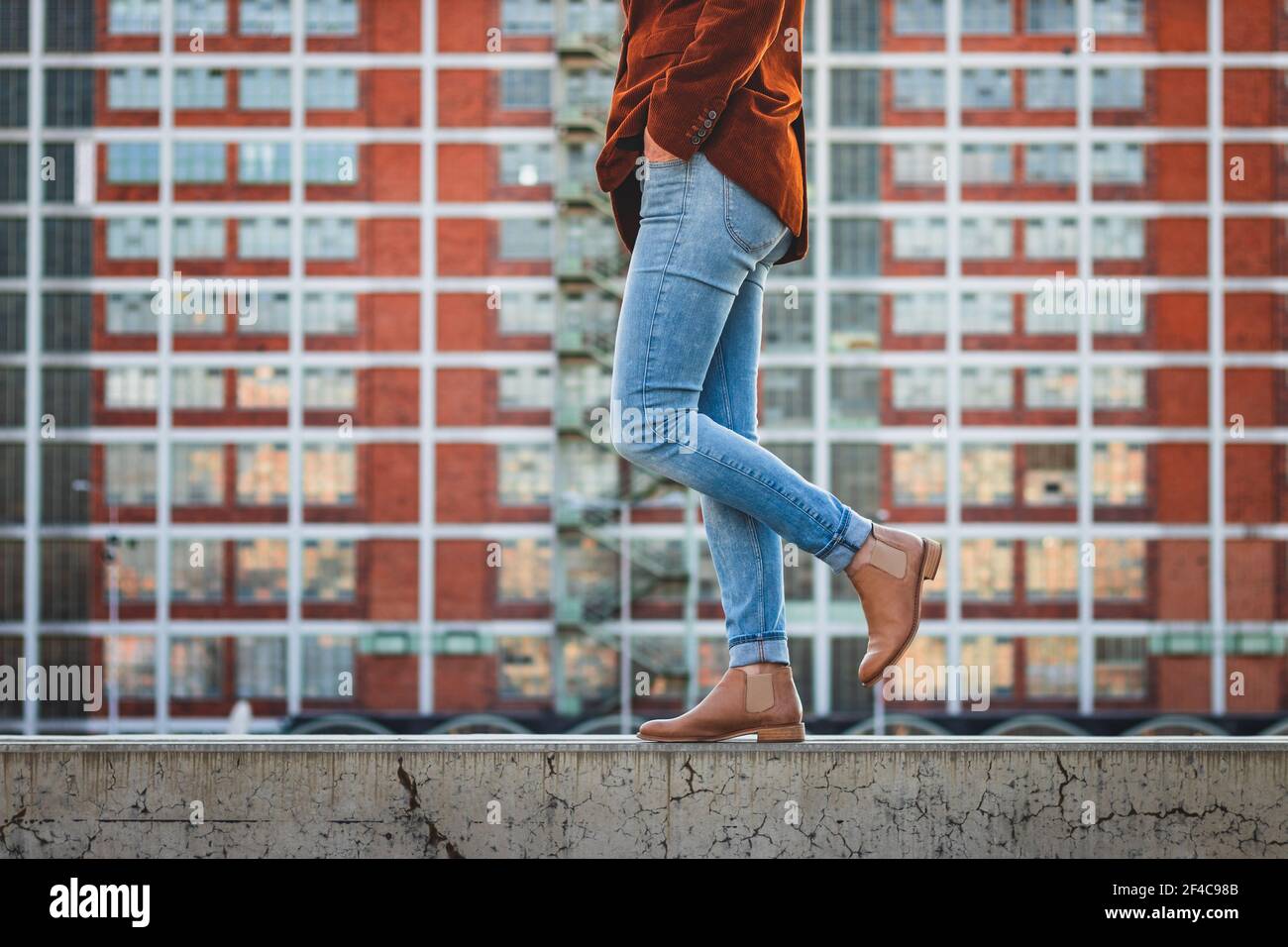 Donna che indossa pantaloni in denim e scarpe eleganti in pelle in città. Architettura moderna come sfondo. Concetto di bellezza e moda Foto Stock