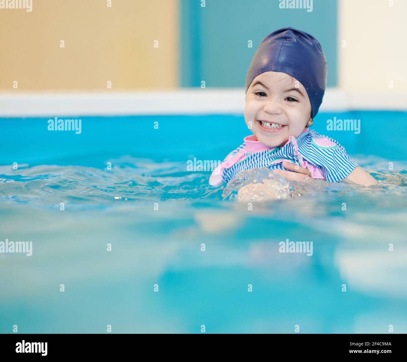 Sorriso di ragazza in piscina su sfondo d'acqua sfocato. Tema delle lezioni di nuoto Foto Stock