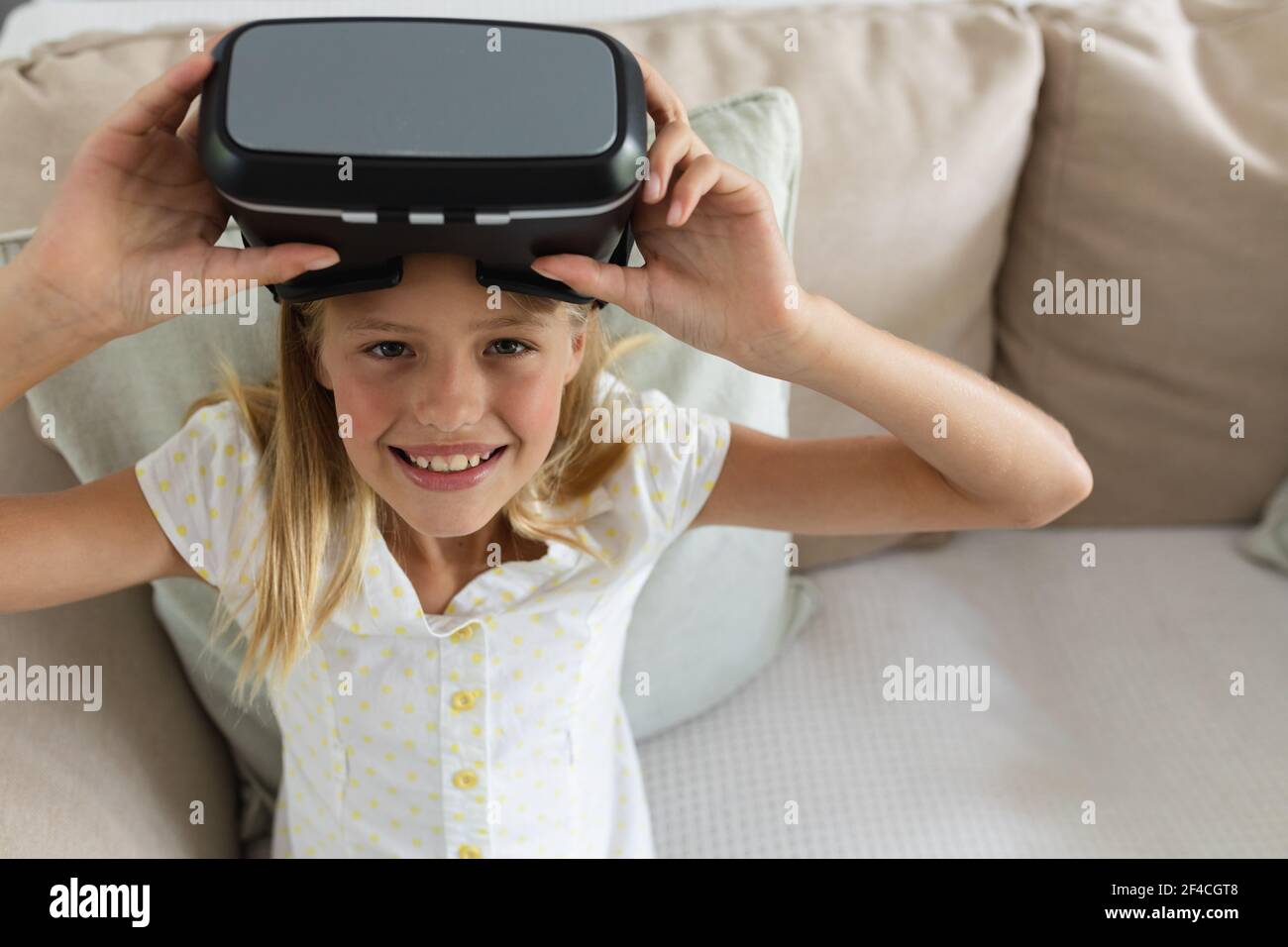 Ritratto di una ragazza caucasica seduta sul divano con visore vr alzandolo e sorridendo Foto Stock