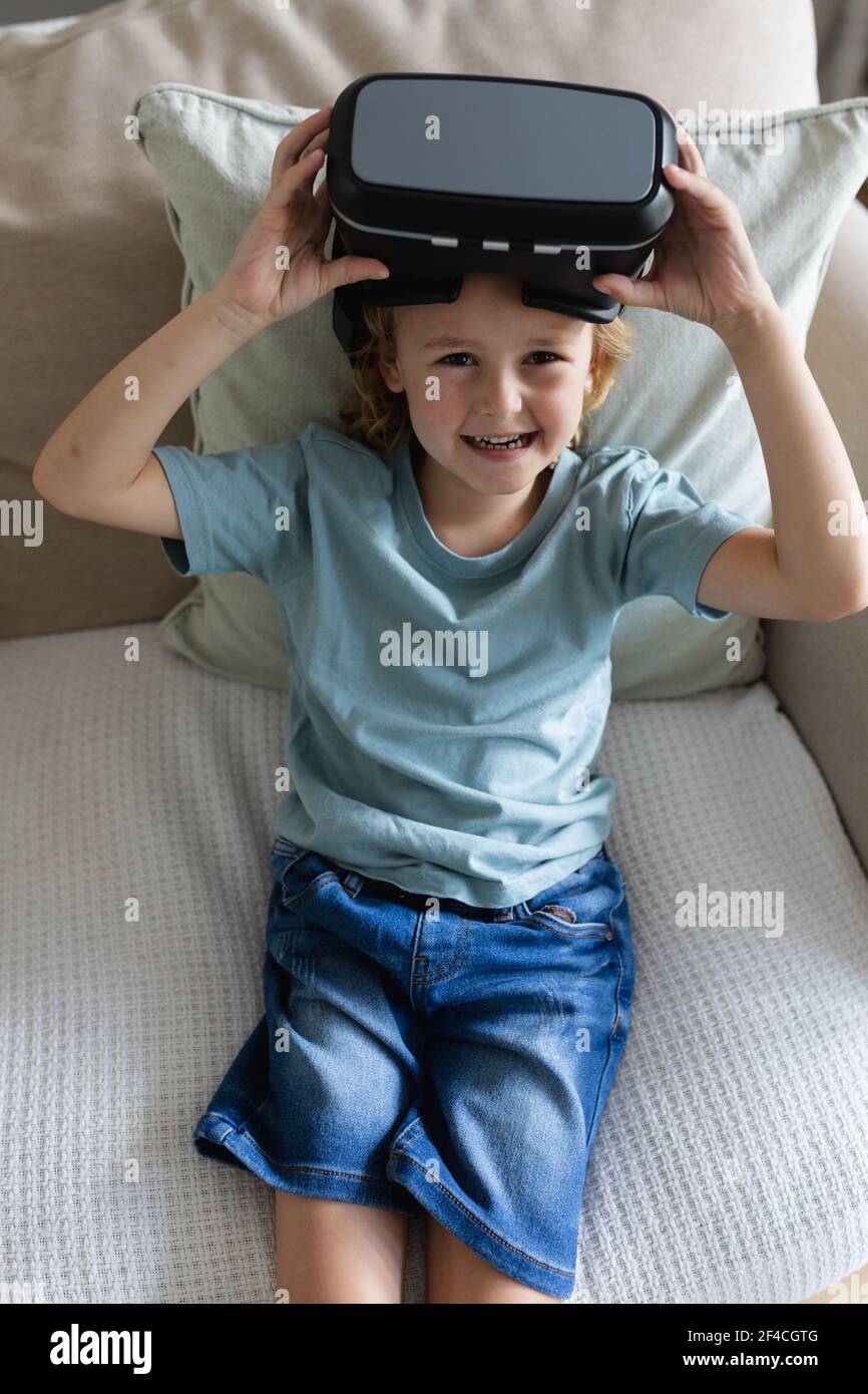 Ritratto di un ragazzo caucasico seduto sul divano con visore vr alzarlo e ridere Foto Stock