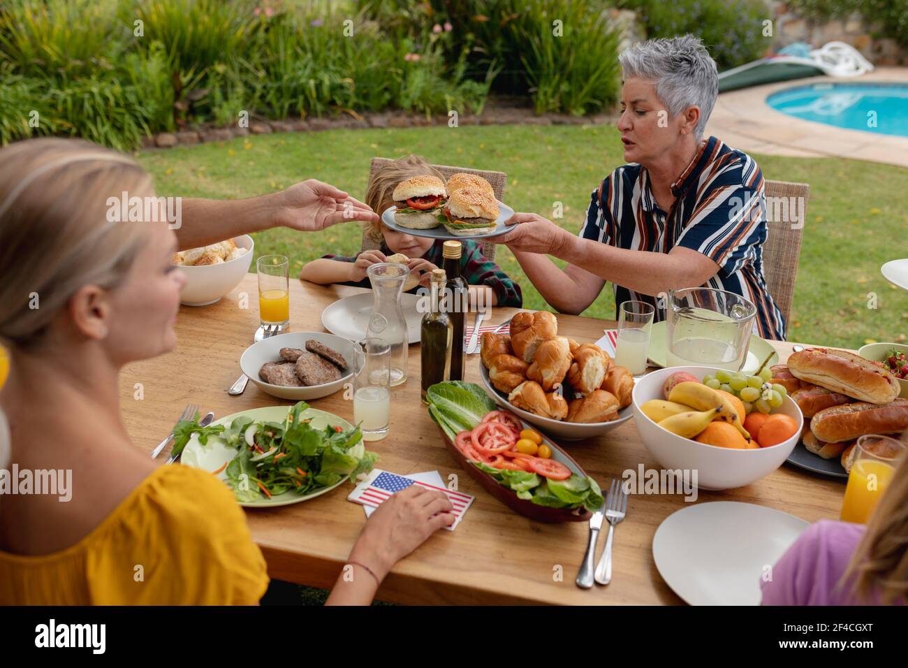 Sorridente anziana caucasica che serve la famiglia prima di mangiare insieme in giardino Foto Stock