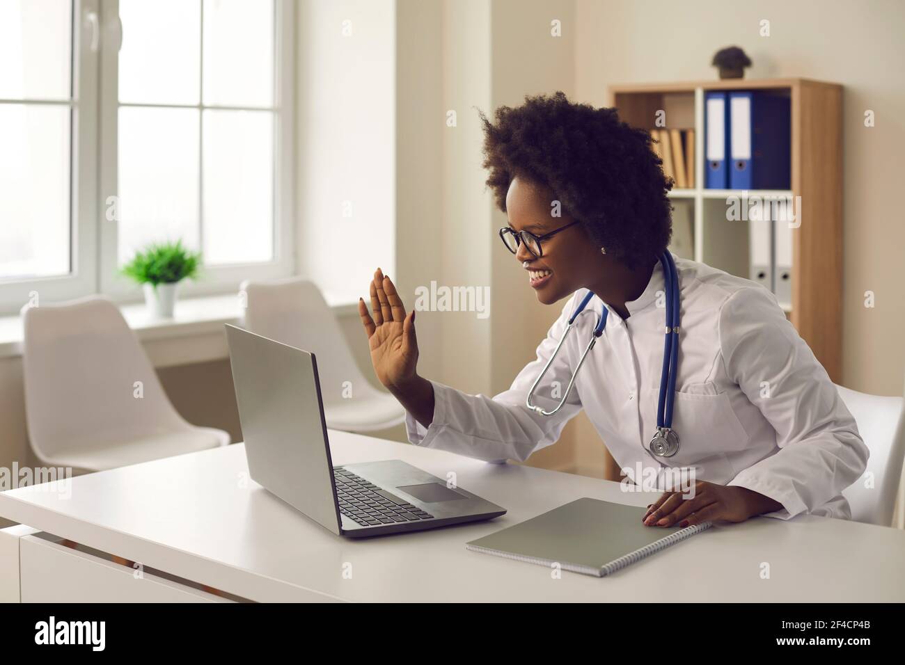 La giovane dottoressa dalla pelle scura fornisce una consultazione online al paziente tramite collegamento video. Foto Stock