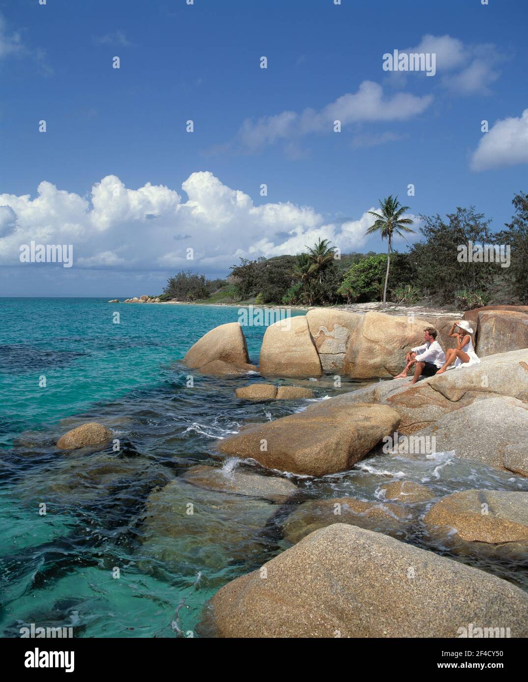 Australia. Queensland. Isola di Lizard. Vista della costa con giovane coppia seduta su rocce. Foto Stock