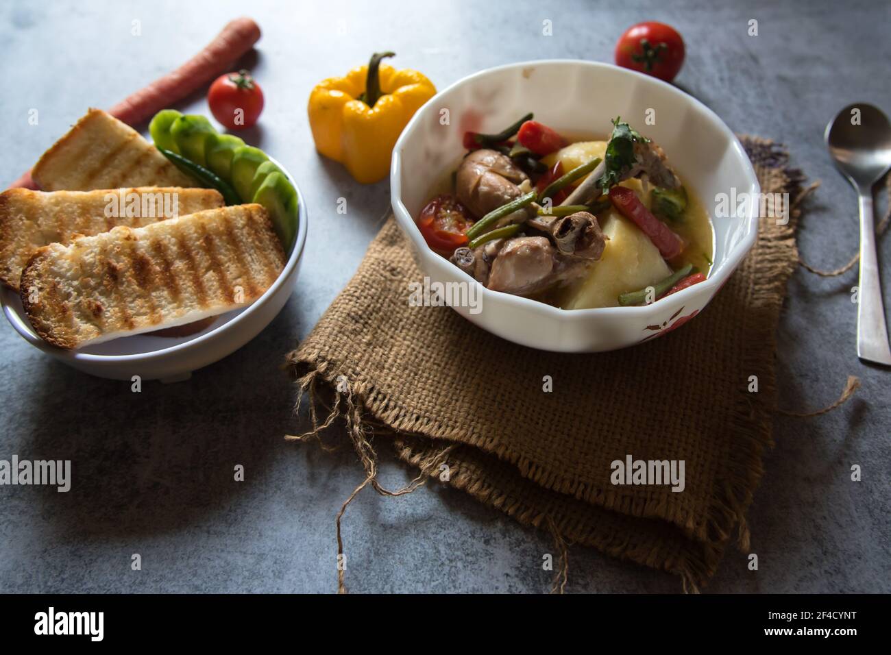 Primo piano di stufato di pollo e verdure in un recipiente e condimenti crudi Foto Stock