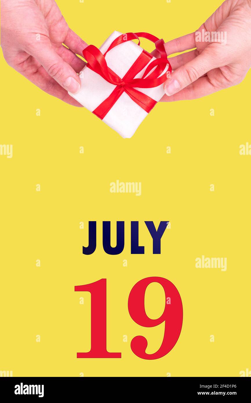 19 luglio. Calendario verticale festivo con mani che tiene bianco scatola regalo con nastro rosso e calendario Data 19 luglio su illuminante giallo background.Sum Foto Stock