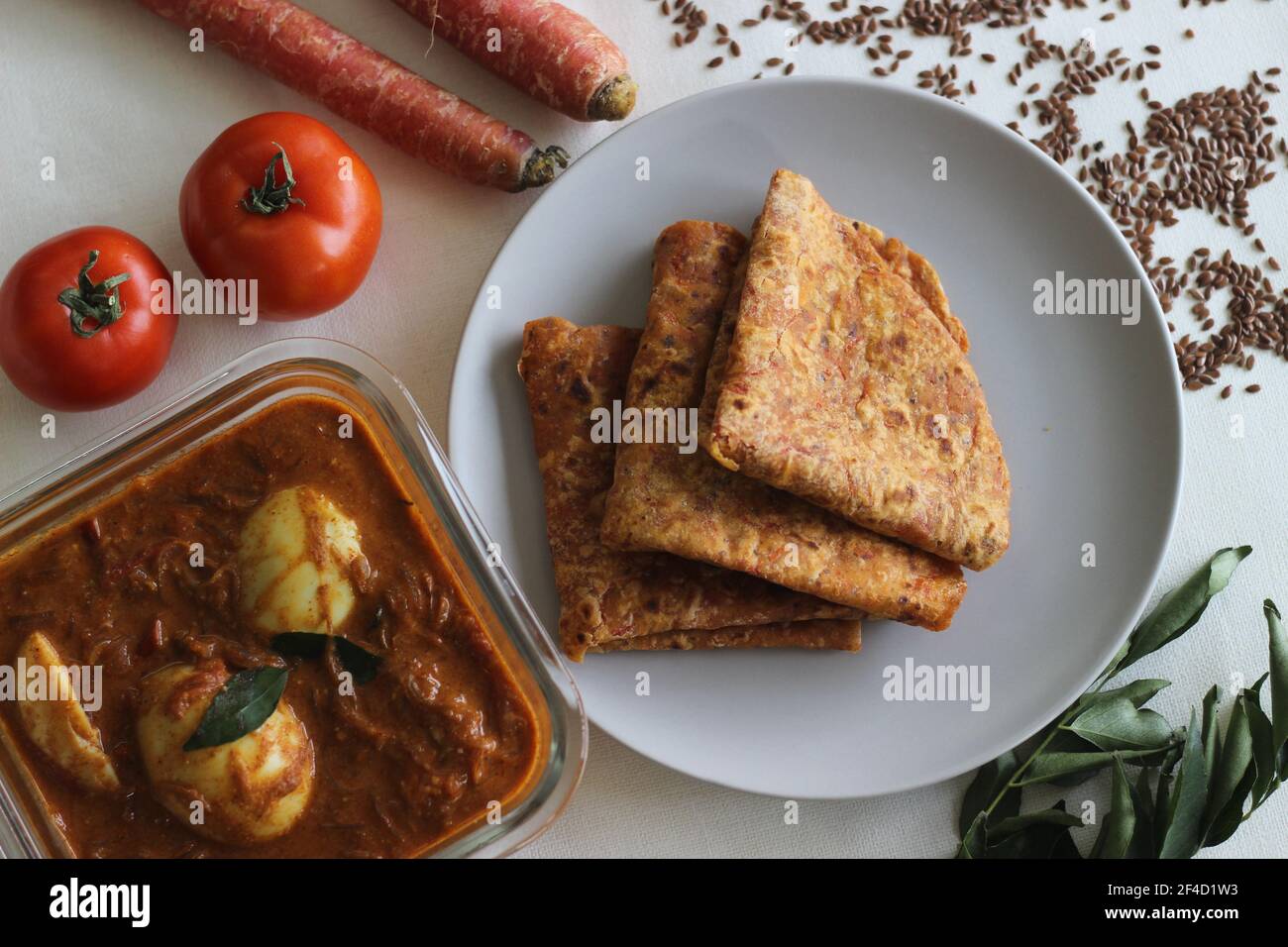 Pane piatto indiano integrale di grano fatto di carote grattugiate e semi di lino in polvere servito con curry d'uovo bollito, un sugo a base di pomodoro di anacardi. Shot su bianco b Foto Stock