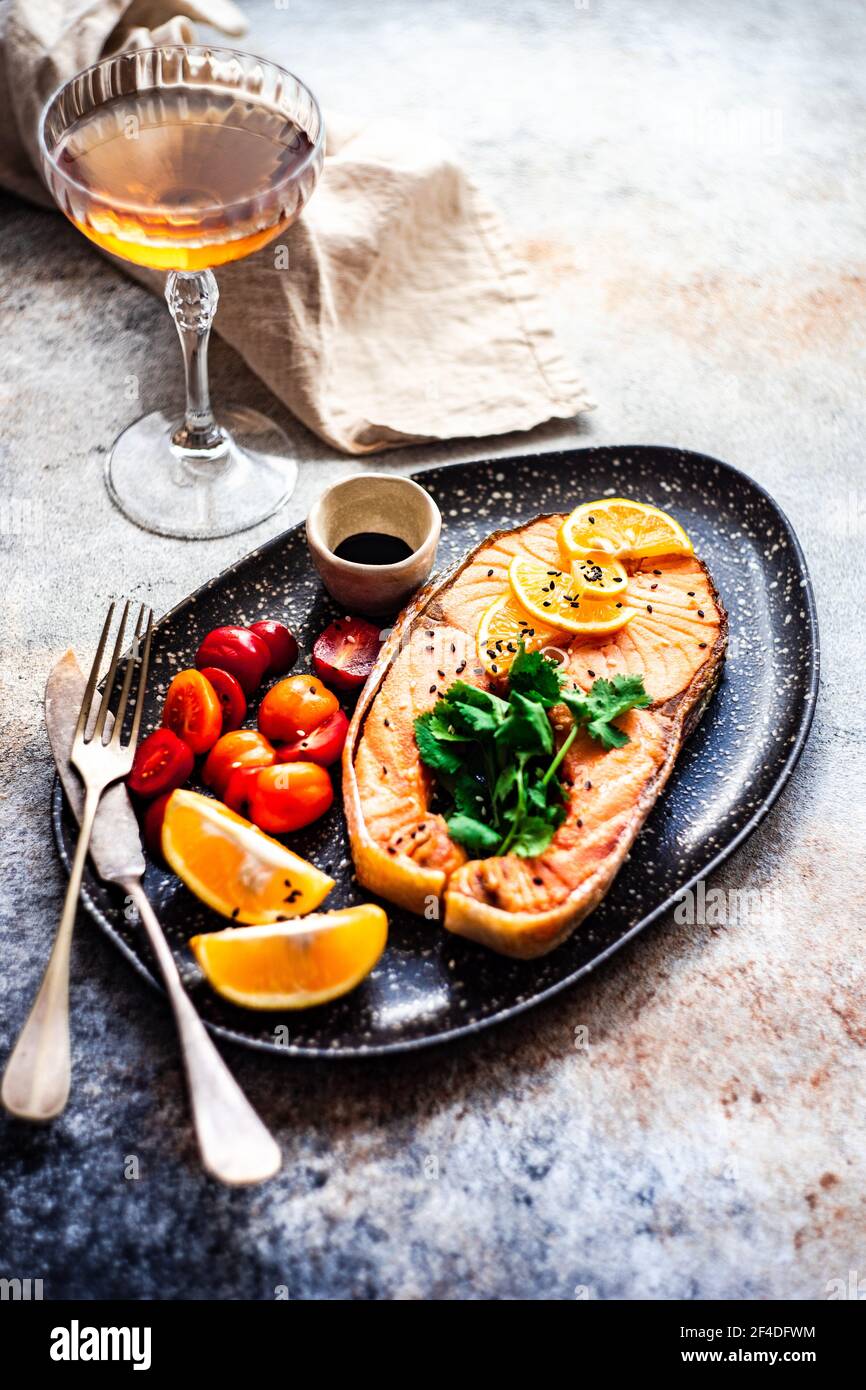 Bistecca di salmone alla griglia con pomodori, limone e un bicchiere di vino bianco Foto Stock