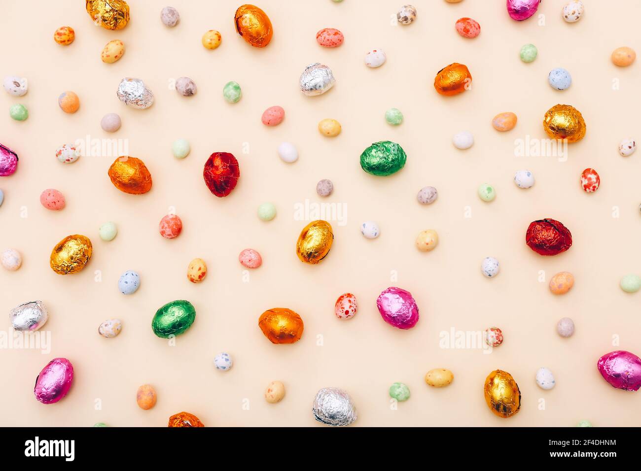 Mini uova di cioccolato pasquale avvolte in un foglio colorato, sparse su uno sfondo beige Foto Stock