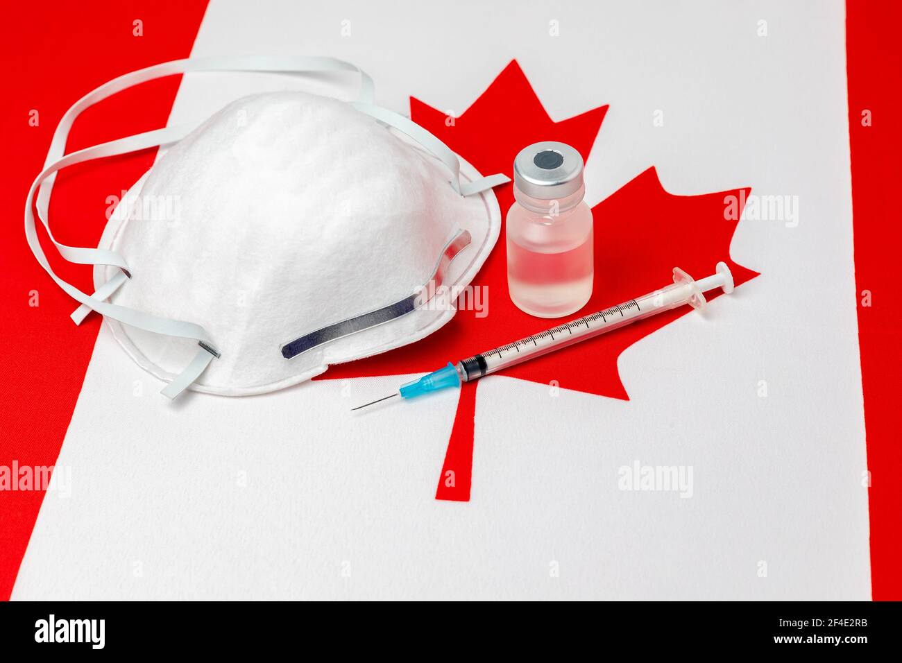 Flag Canada, maschera facciale N95, siringa con ago e flaconcino. Concetto di distribuzione del vaccino del coronavirus Covid-19, carenza di approvvigionamento e crisi sanitaria Foto Stock