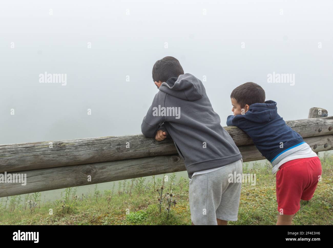 colpo orizzontale di due bambini appoggiati su una recinzione di legno guardando la nebbia Foto Stock