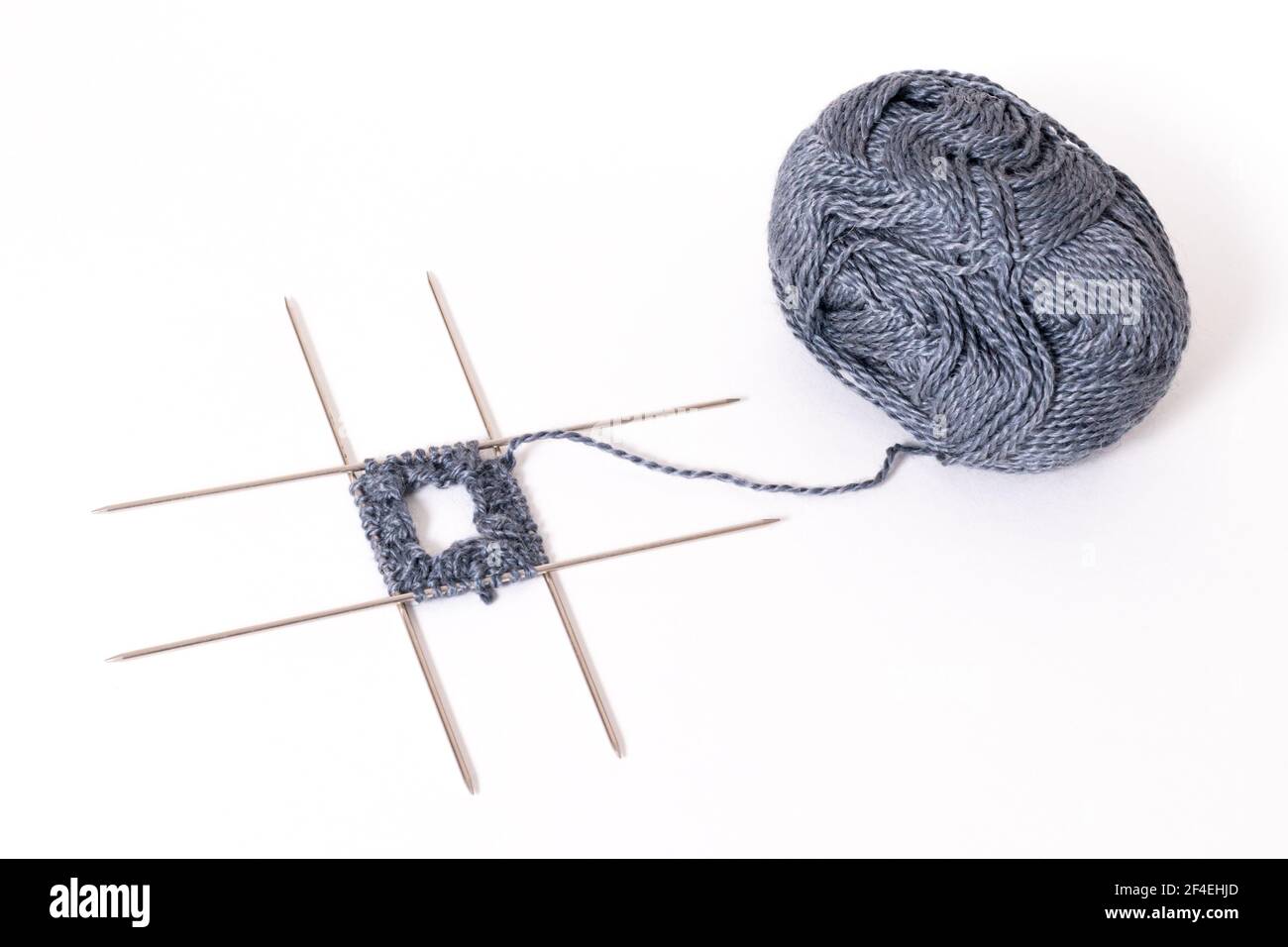 Iniziare a lavorare a maglia su quattro aghi da maglieria. Aghi per maglieria e lana isolati su sfondo bianco Foto Stock