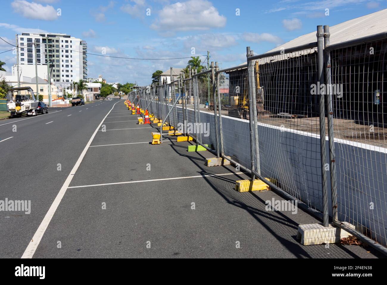 Una linea di recinzioni temporanee con basi gialle in cemento erette di fronte ad un sito di demolizione in una città regionale. Foto Stock