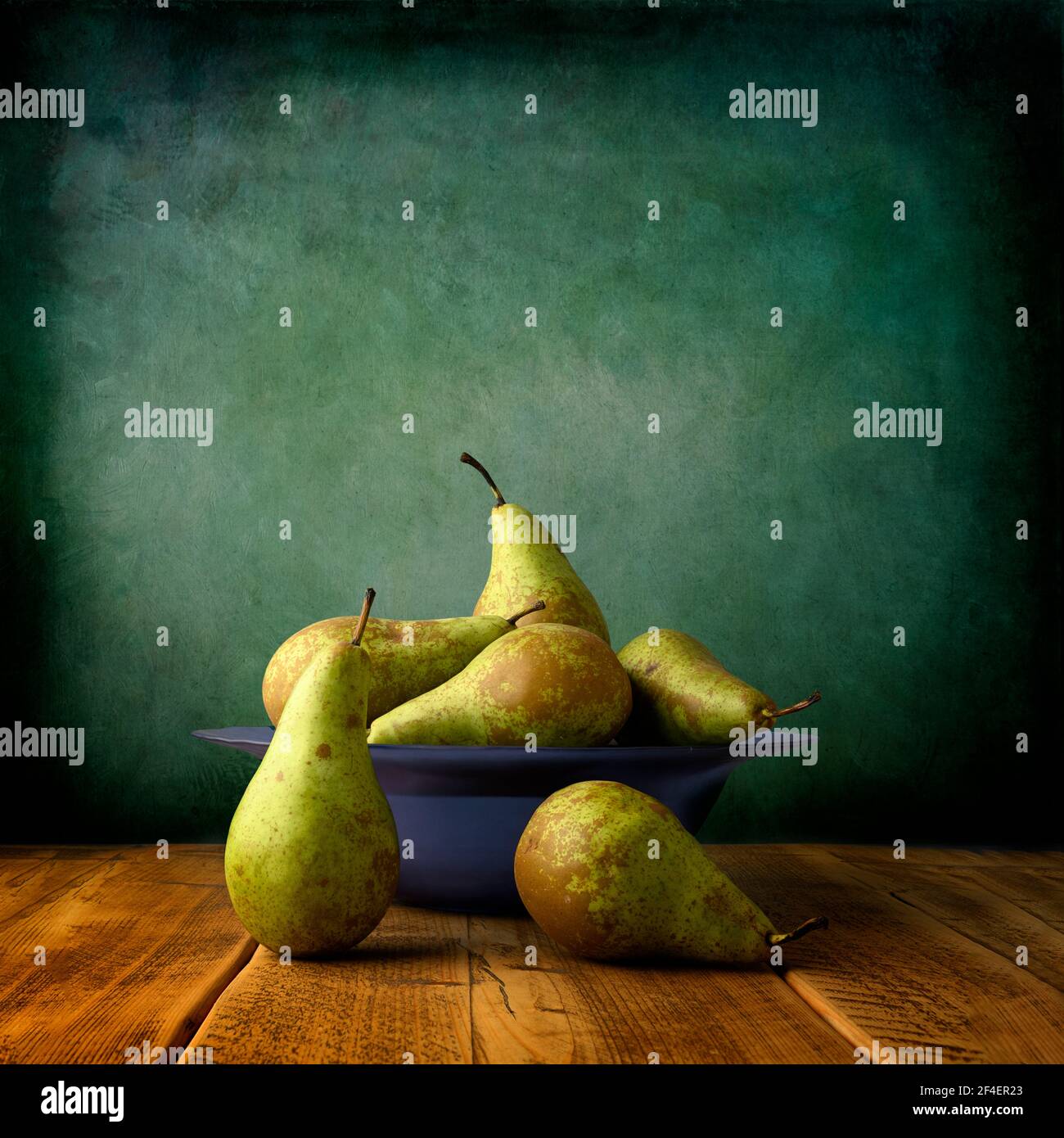 Sei pere da conferenza fresche disposte in un vetro blu chiaro ciotola posta su un tavolo di quercia planata e fotografata contro sfondo blu/verde Foto Stock