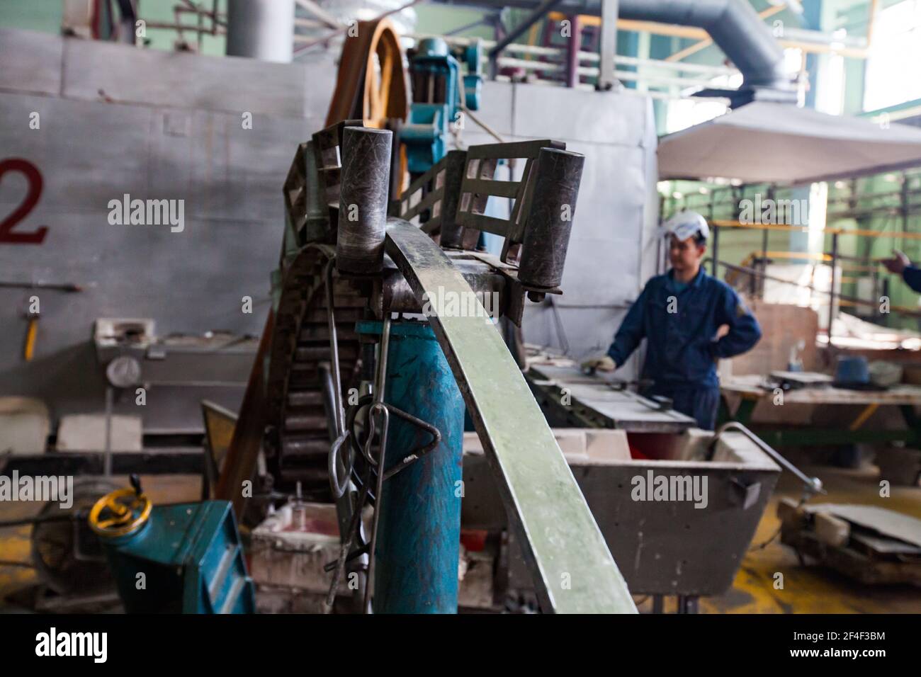 Pavlodar, Kazakhstan - Maggio 29 2012: Macchina per la produzione di aste e operatore in maschera protettiva in vetro (destra, sfocata). Asta e cavo in alluminio Foto Stock