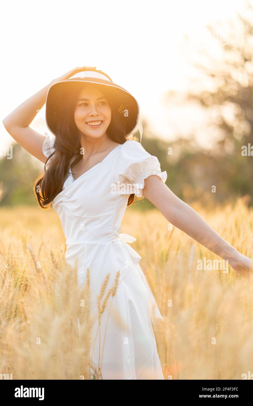 Felice giovane bella donna che indossa cappello nero e vestito bianco  godendosi a piedi nel campo d'orzo d'oro su un tardo pomeriggio,  retroilluminato, camera Foto stock - Alamy