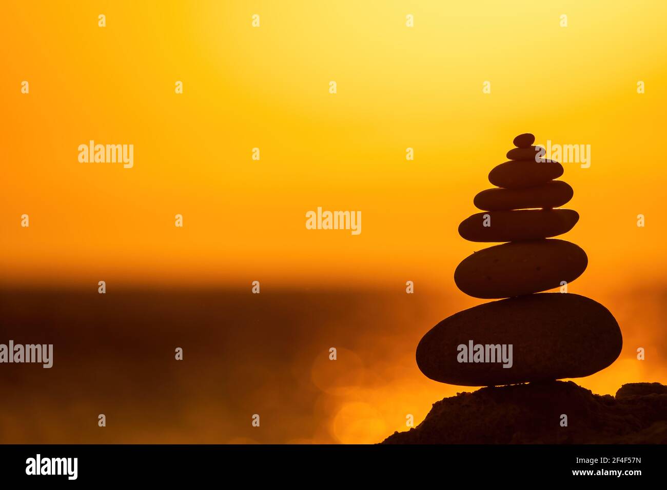 Profilo a piramide di ciottoli bilanciato sulla spiaggia. Astratto caldo tramonto bokeh con Mare sullo sfondo. Pietre Zen sulla spiaggia di mare, meditazione, spa Foto Stock