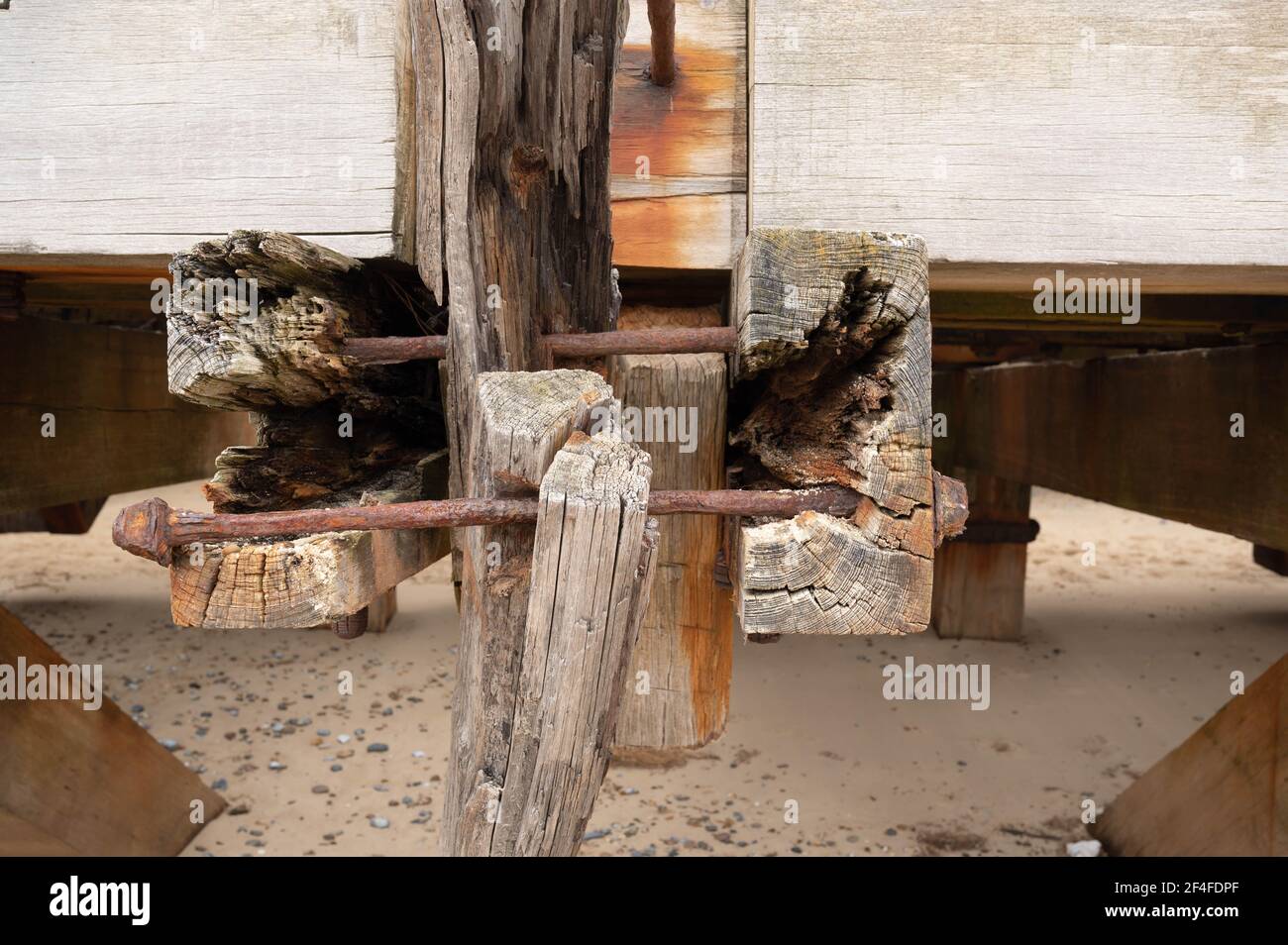 Travolgente travi di legno alla fine di un molo in inghilterra norfolk, dove l'aria e l'acqua di mare salato ha eroso e arrugginito tutti i dadi e bulloni grandi. Foto Stock